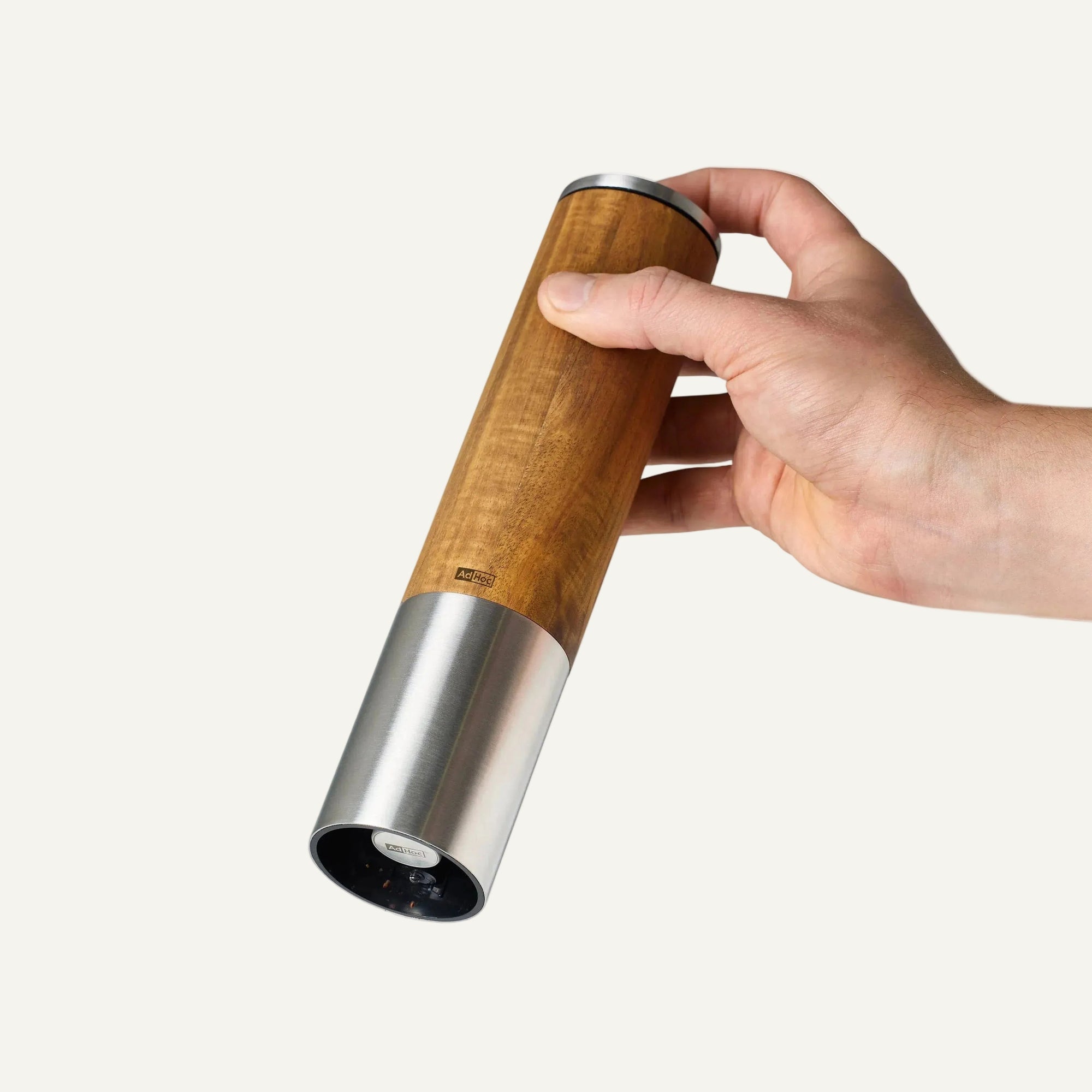 Hand holding a wooden pepper grinder with salt being sprinkled on a white background